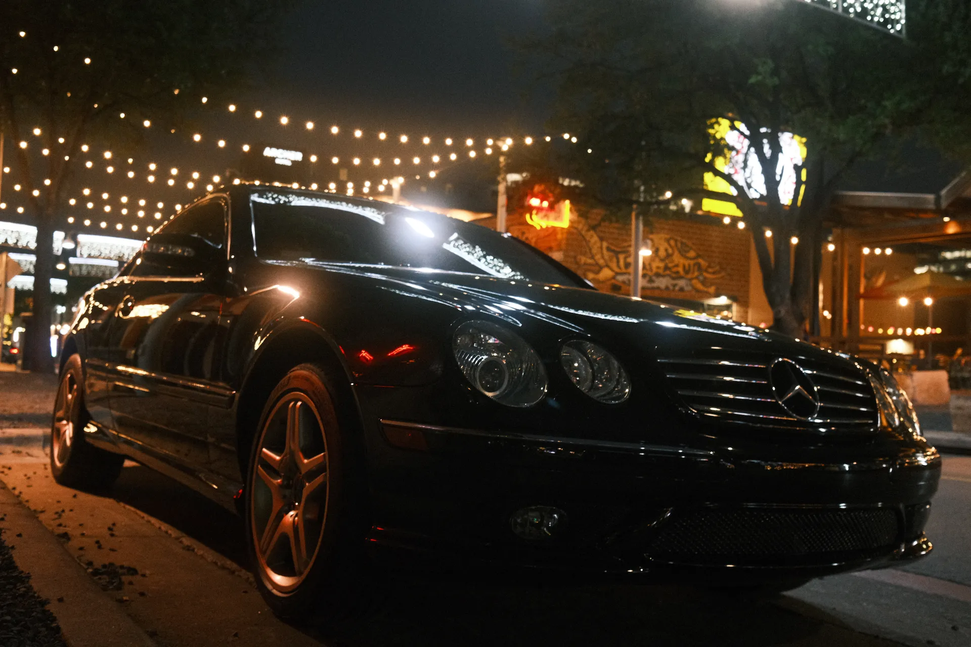 A black mercedes parked under some street lights